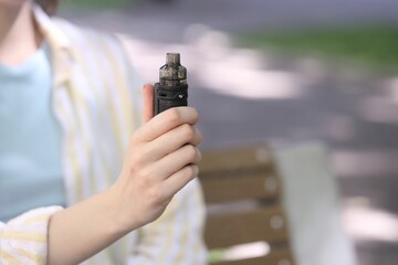 Young woman with electronic smoking device outdoors, closeup. Space for text