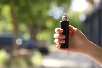 Young woman with electronic smoking device outdoors, closeup. Space for text