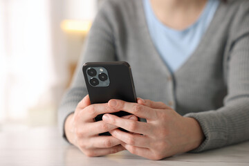 Woman using smartphone at table indoors, closeup