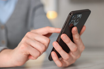 Woman using smartphone at table indoors, closeup