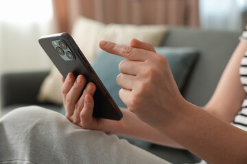 Woman using modern smartphone on sofa at home, closeup