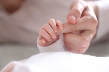 Fototapeta premium Mother holding her baby's hand indoors, closeup