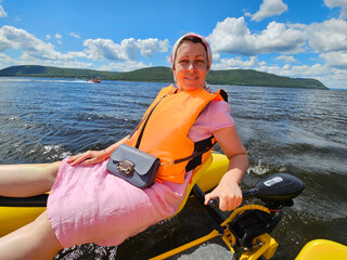 Woman wearing a pink dress and an orange life jacket is sitting on a yellow boat inflatable...