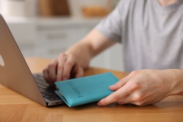 Man with passport using laptop at wooden table indoors, closeup