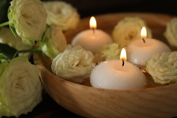 Burning candles, water and rose flowers in bowl on wooden table, closeup