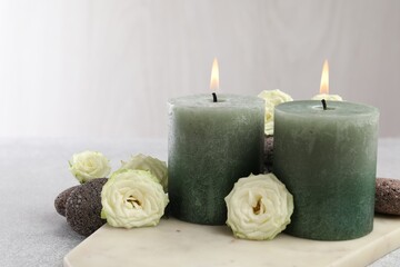 Burning candles, stones and rose flowers on light grey table, closeup