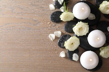 Burning candles, stones and rose flowers on wooden table, flat lay. Space for text