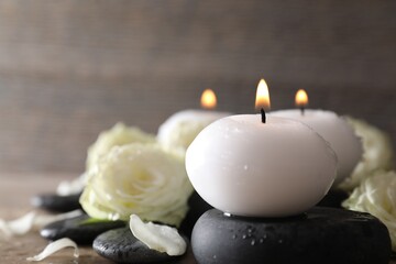 Burning candles, stones and rose flowers on wooden table, closeup
