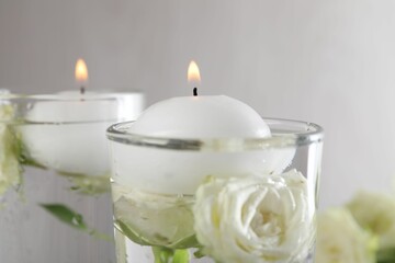 Burning candles in glasses with water and rose flowers on table, closeup