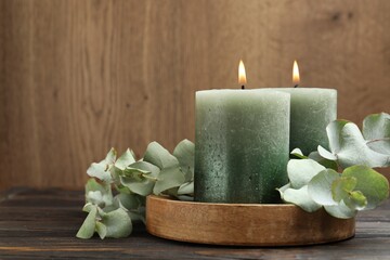 Burning candles and eucalyptus branches on wooden table, closeup. Space for text