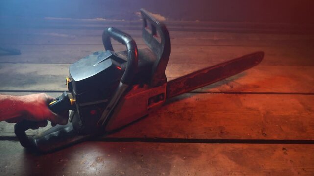 A man starts a black and orange chainsaw in a dark room for testing