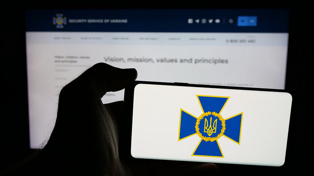 Stuttgart, Germany - 06-18-2025: Person holding mobile phone with logo of security service Sluzhba Bezpeky Ukrainy SBU on screen in front of web page. Focus on phone display.