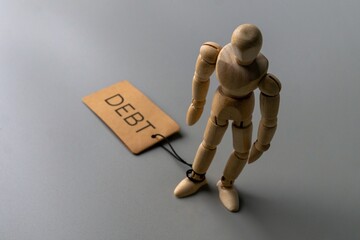 A wooden figure stands with one ankle tied by a string to a tag labeled 
