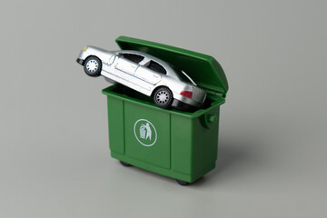 A toy car inserted into a green trash bin. Vehicle disposal, car write-offs, old car issues,...