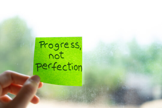 Hand holding sticky note with progress not perfection reminder