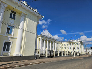 Fototapeta premium Large building Office of the Federal Security Service for the Kostroma Region with a white facade and a red and white flag on top. The building has a lot of columns and is surrounded by a sidewalk