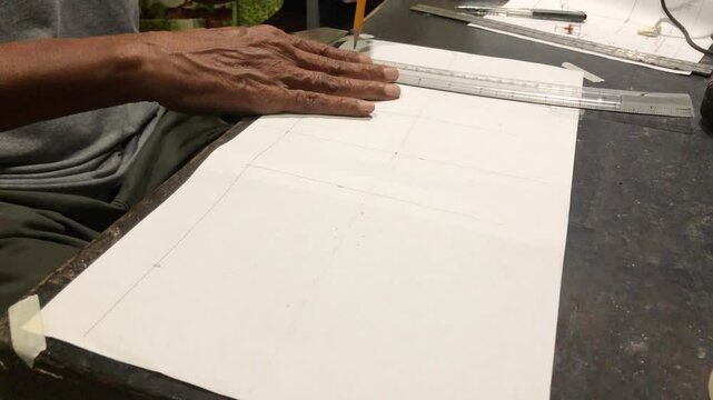 man is drafting a house plan using a pencil and T-square on a piece of bond paper at his desk.