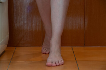 Bare feet of a young girl in the bathroom in an apartment on tiles in the morning, feet