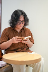 A young Chinese man in his early twenties, wearing glasses, sits in a stylish cafe, deeply focused...
