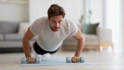 Caucasian man doing pushups with dumbbells at home living room. Morning fitness workout exercise routine. Indoor sport and healthy lifestyle concept for personal training - Powered by Adobe