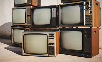 Antique retro old televisions pile on floor in front of old wall background. Vintage style photo with blank screen display.