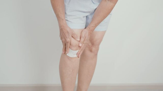 Elderly woman having knee ache with Medicated pain relief patch plaster to Runners Knee or Patellofemoral Pain Syndrome, osteoarthritis, arthritis, rheumatism and Patellar Tendinitis. Senior health