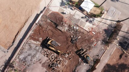 Bird's eye aerial descending spiral shot of a heavy excavator and small dozer removing contaminated debris after the Eaton Fire in Altadena, California. 4K