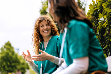 Two healthcare professionals engaged in lively conversation at a park during a sunny day in the...
