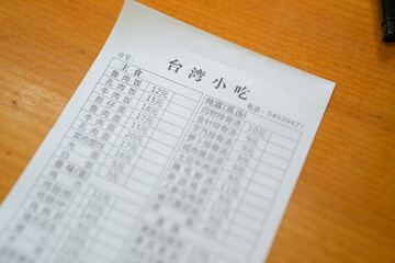 A Taiwanese restaurant order sheet is placed on a wooden table, showing handwritten marks beside...