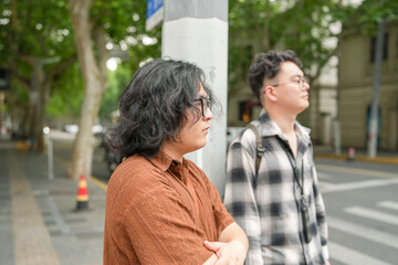 Two Chinese men in their early twenties, both wearing glasses, walk together along a wide and busy...