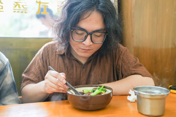Two young Chinese men in their early twenties, both wearing glasses, are eating lunch together at a...