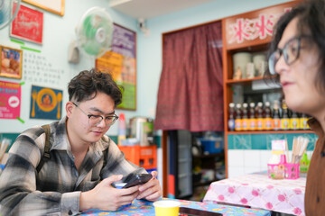 Two Chinese men in their early twenties, both wearing glasses, are casually waiting at a Thai...