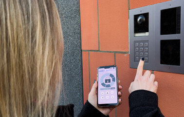 Young stylish woman getting access to the building by attaching smartphone to intercom. Concept of...