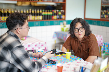 Two Chinese men in their early twenties, both wearing glasses, are casually waiting at a Thai restaurant for their meal to be prepared on a pleasant spring day in Huangpu District, Shanghai, China.