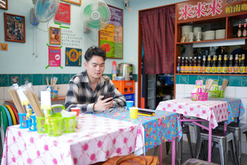 Two Chinese men in their early twenties, both wearing glasses, are casually waiting at a Thai...