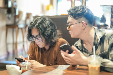 Two young Chinese men in their early twenties, both wearing glasses, are drinking beverages, using...