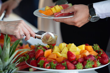 Waiter serving sliced fruits to guests at a buffet