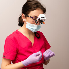 Skilled dentist in pink scrubs performing delicate procedure with precision tools under...