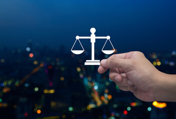 Hand holding law flat icon in fingers over blur colorful night light modern city tower and skyscraper, Business legal service concept