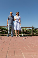 Blind woman walking with white cane and friend in park