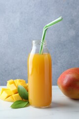 Tasty mango juice in glass bottle, fresh fruits and green leaves on white marble table