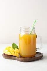 Tasty mango juice in glass mason jar, fresh fruit and mint on white table