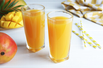 Tasty mango juice in glasses, fresh fruits, straws and green leaves on white wooden table, closeup