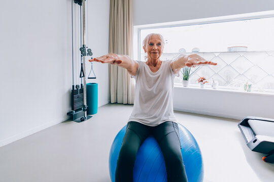 Senior woman doing arm exercises with fitness ball in home gym