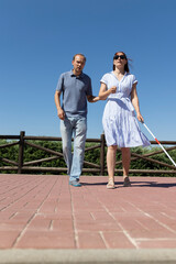 Man guiding blind woman with white cane walking in park