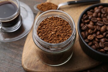 Instant coffee in glass jar, hot drink and beans on wooden table, closeup