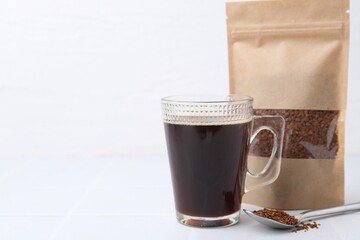 Instant coffee in bag, spoon and cup of drink on light table. Space for text
