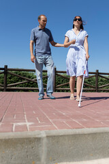 Man helping blind woman walking with white cane on sidewalk