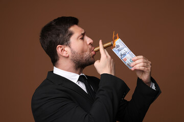 Greedy businessman lighting cigar with dollar banknote on brown background