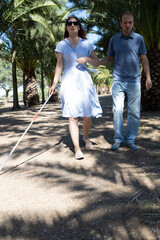 Fototapeta premium Blind woman walking with white cane and friend in park
